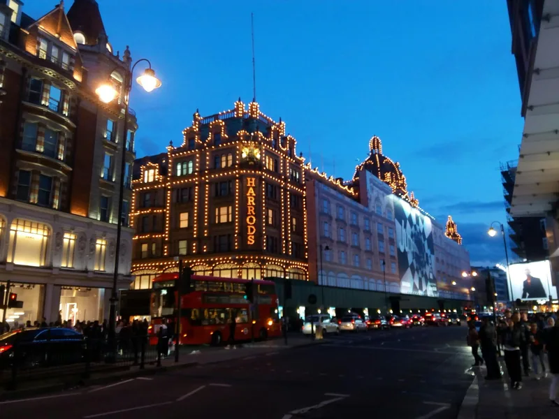 Harrods outlined in thousands of lights at dusk, with a red bus waiting outside