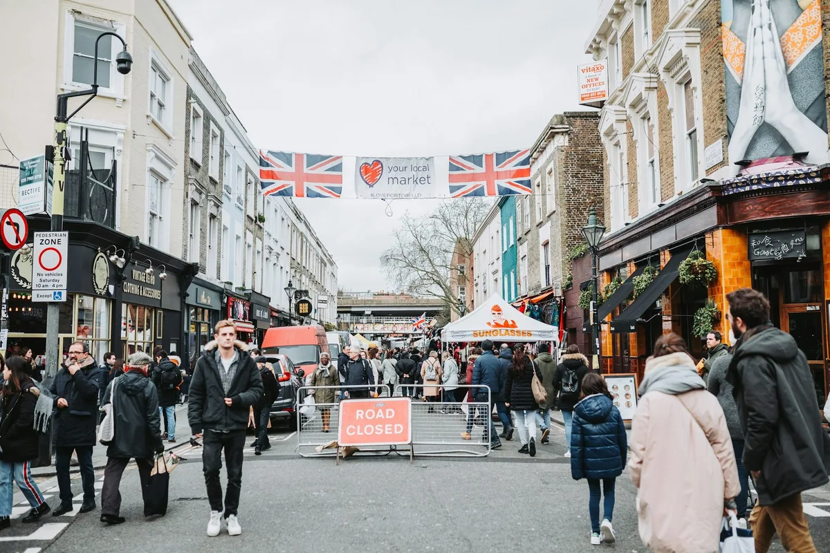 Crowds on Portobello Road below Union Jack market banners, with pastel terraces on both sides