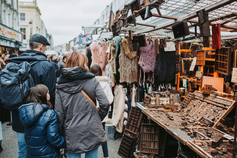 Shoppers browsing antique tools and vintage clothing at stalls on Portobello Road