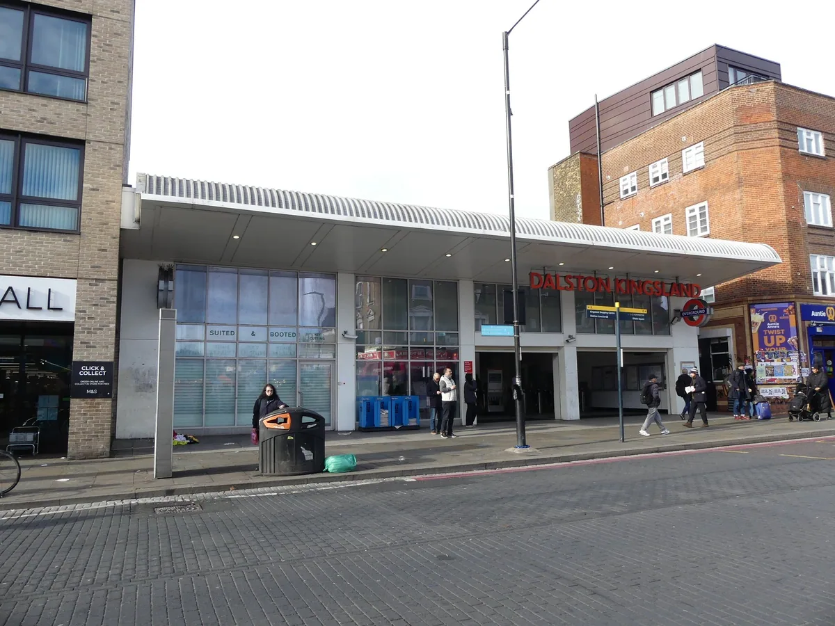 The low canopied front of Dalston Kingsland station on Kingsland High Street, the street the market runs off, with shoppers on the pavement