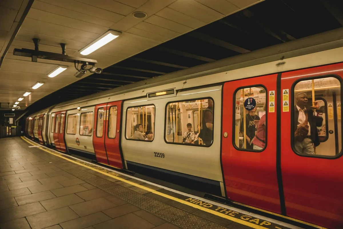 A red, white and blue London Underground train standing at a quiet platform under bright station lights