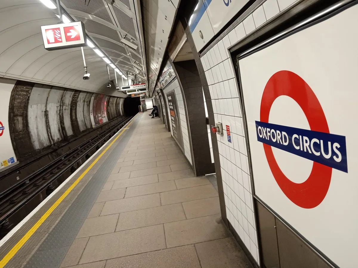 A quiet tiled platform at Oxford Circus tube station, with the station roundel on the wall and a train waiting