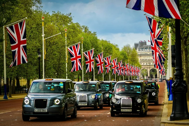 Line of black cabs driving along The Mall beneath rows of Union Jack flags