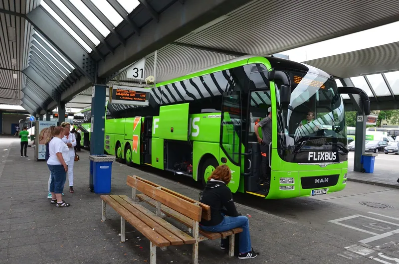 A long-distance coach waiting at a covered departure stand while passengers sit and wait nearby