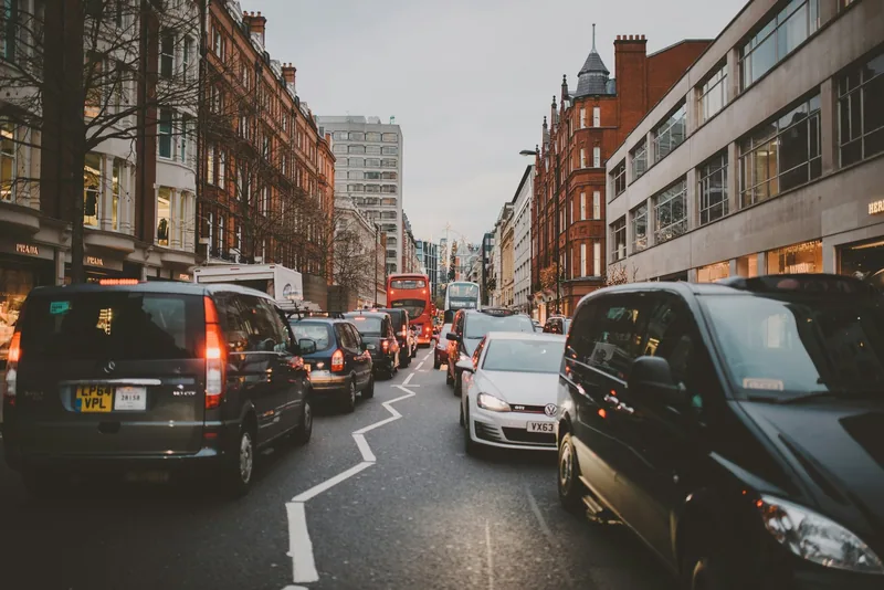 Cars and vans queueing along a busy London street lined with red-brick buildings