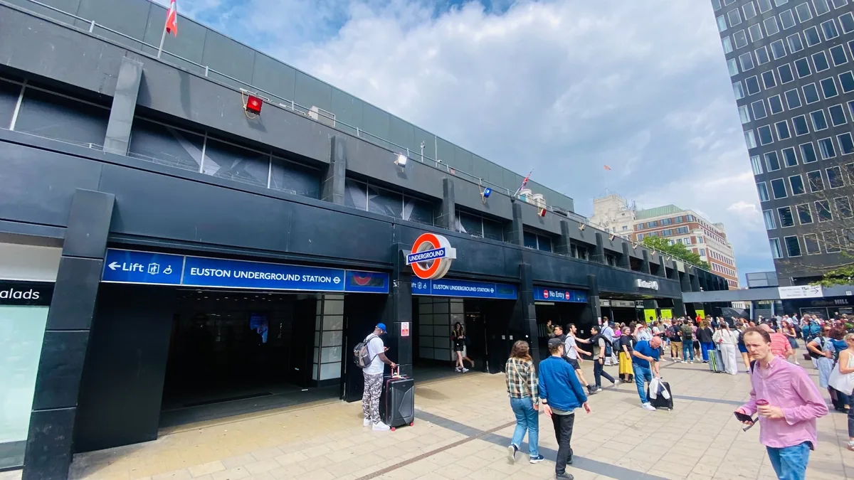 The Euston station forecourt with the Underground entrance and roundel, travellers crossing with cases