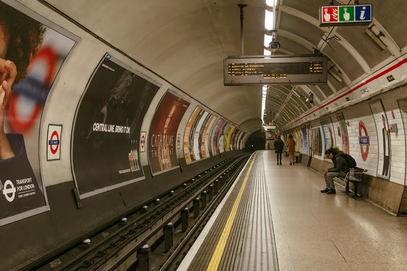 A single passenger waits on a quiet curved tube platform under a London Underground roundel