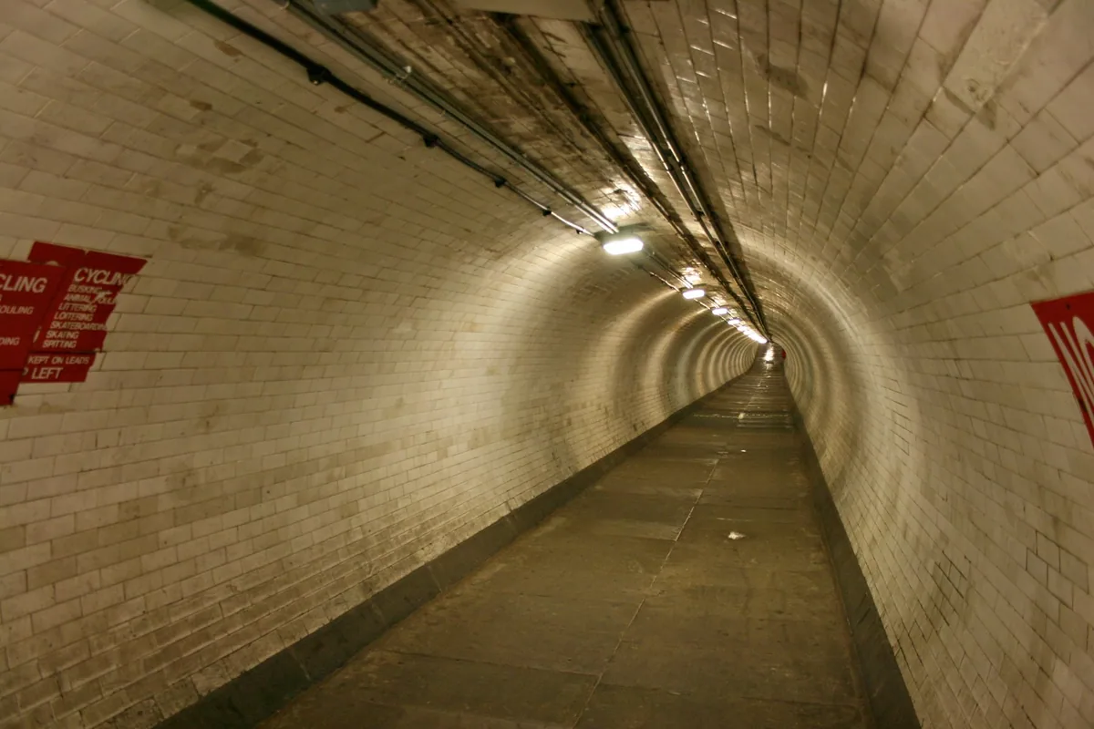 The white-tiled Greenwich Foot Tunnel curving away under the Thames, lit by strip lights