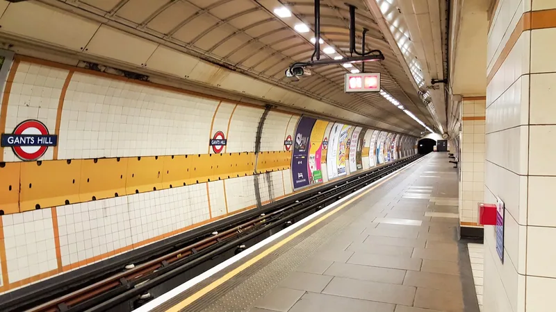 An empty Central line platform at Gants Hill, Gants Hill roundels along the cream and orange tiled tunnel wall