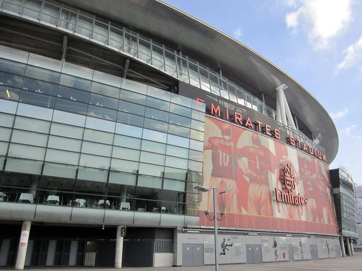 Glass-and-steel exterior of the Emirates Stadium, with a red mural across the upper facade