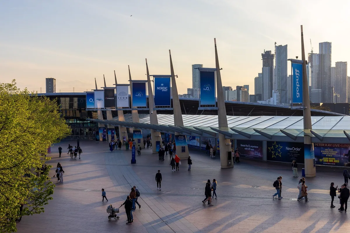 People crossing Peninsula Square towards the North Greenwich station canopy at sunset