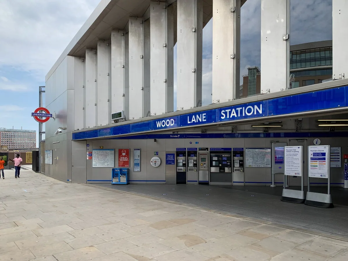 The front of Wood Lane Underground station, with a row of ticket machines under the canopy and the roundel on a pole outside