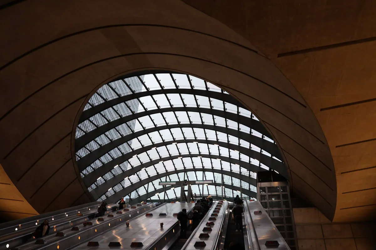 Escalators rising to the curved glass canopy of Canary Wharf Underground station on the Jubilee line