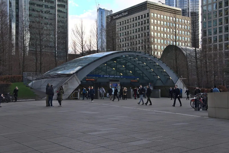 The glass shell entrance to Canary Wharf tube station, with office towers rising behind it