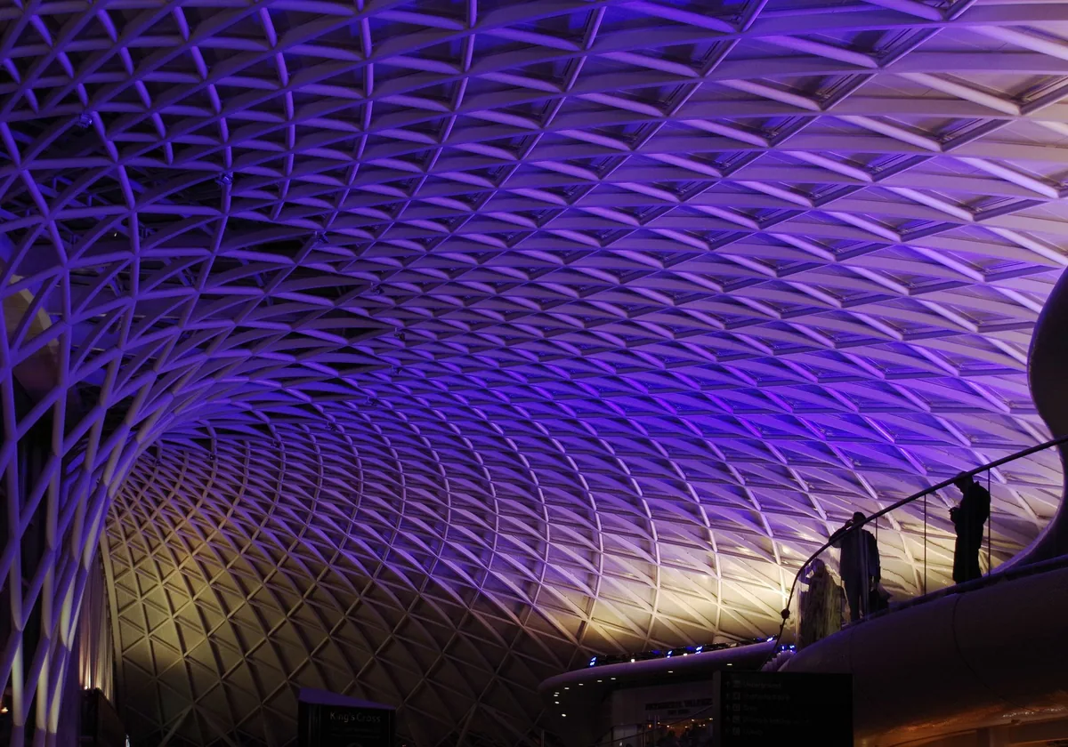 The white lattice roof of the King's Cross western concourse, lit purple after dark