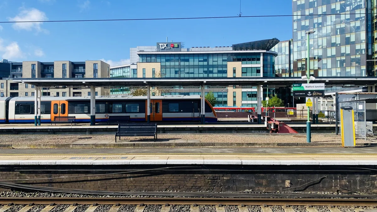 A London Overground train with orange doors standing at the Watford Junction platforms, the station nameboard beside it