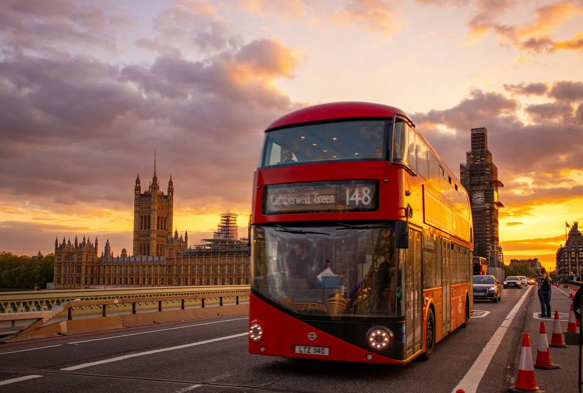 Red double-decker bus on route 148 crossing Westminster Bridge at sunset, the Houses of Parliament behind
