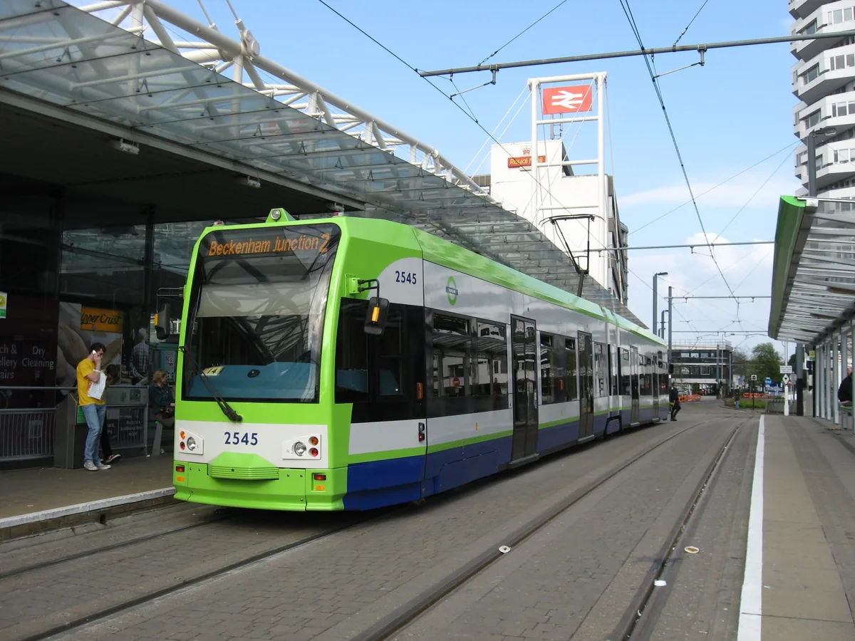A green and white Croydon tram waiting at the stop outside East Croydon station