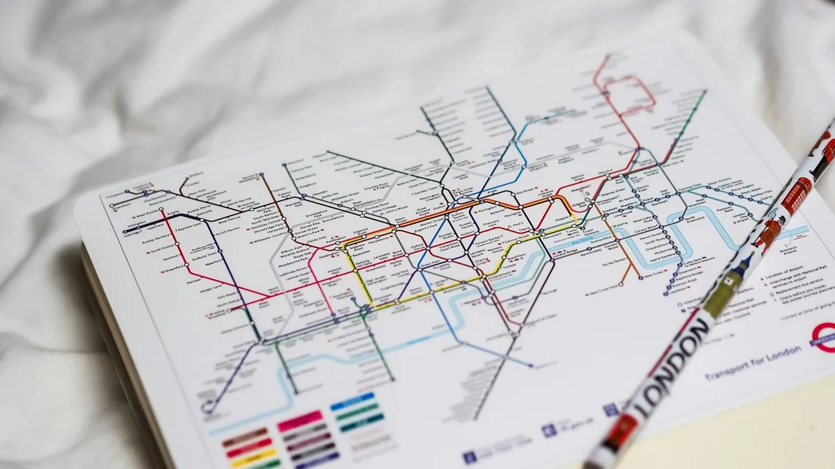 Printed London Tube map with its coloured lines lying open on a white sheet beside a pen