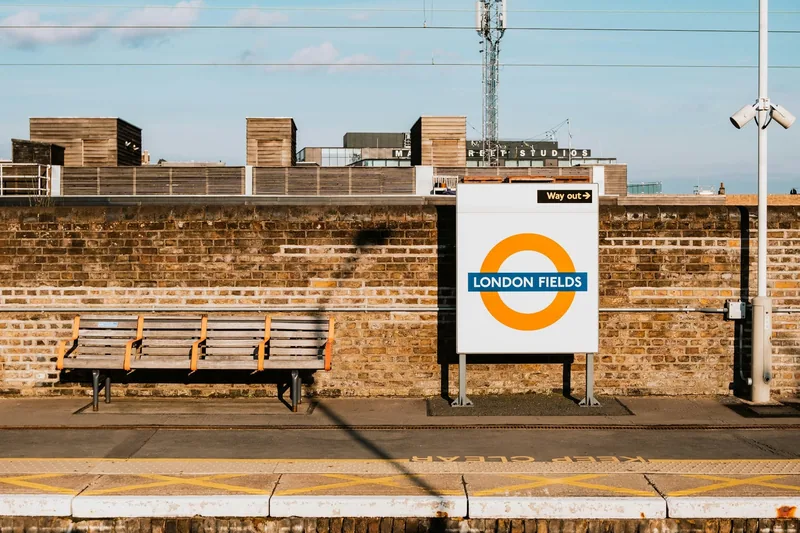 Quiet platform at London Fields station with wooden benches and an orange Overground roundel