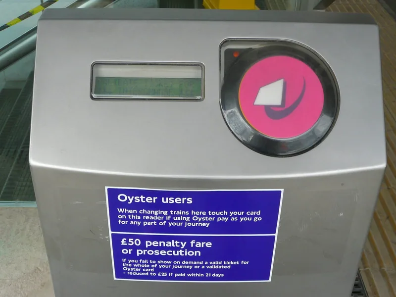 Pink Oyster route validator card reader at a London station with a notice for Oyster users