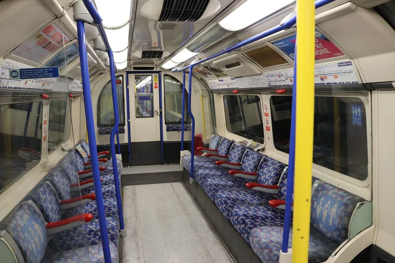 Empty blue moquette seats and grab poles inside a Piccadilly line tube carriage