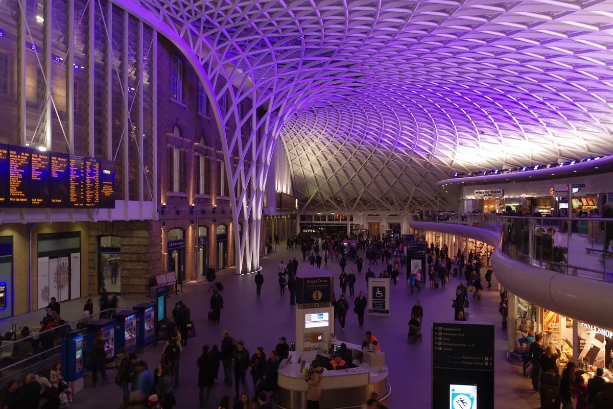 The vaulted western concourse of King's Cross station with departure boards and passengers below