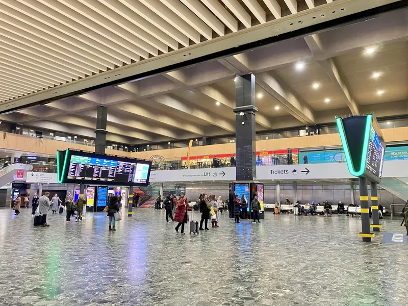 Passengers waiting on the concourse at Euston station beside a sign pointing to the ticket office