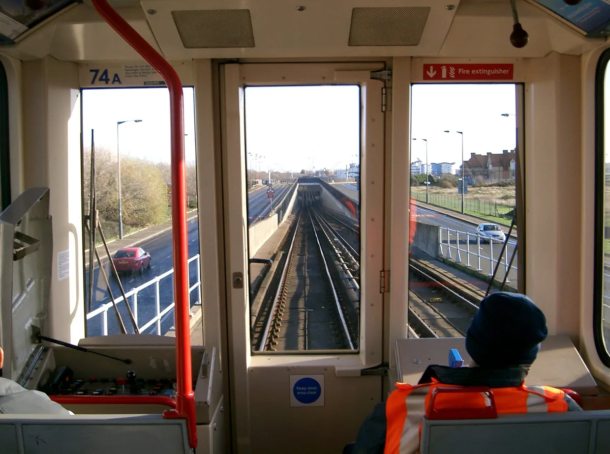 The view forward from the front seat of a DLR train, track running straight ahead and the staff control panel folded shut on the left