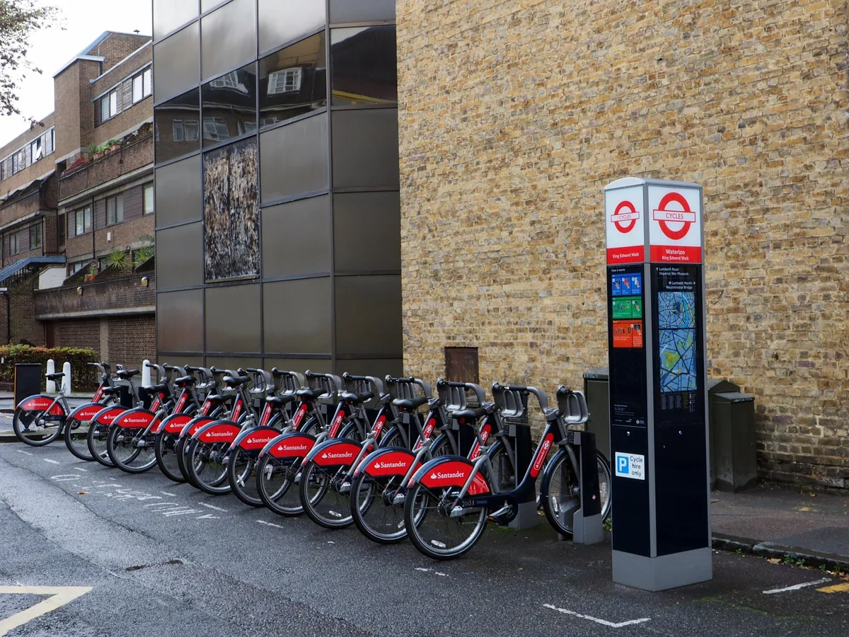 A rack of red hire bikes docked beside the payment terminal at a London cycle hire station