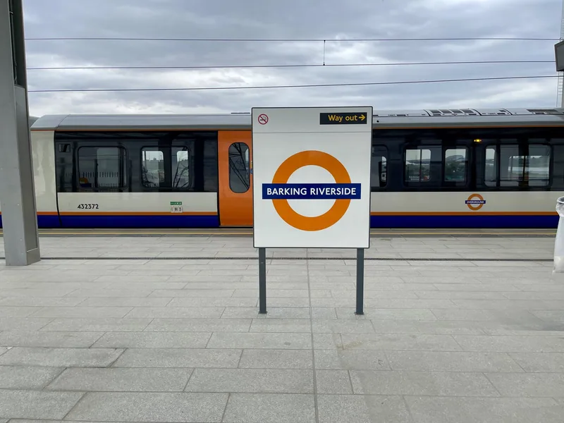 A Barking Riverside roundel sign on the empty platform, with an Overground train standing alongside