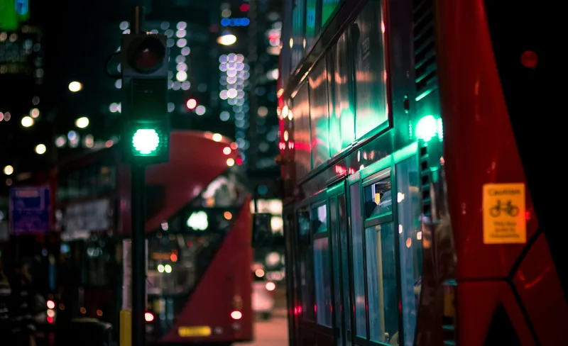 Red double-deckers waiting at a green traffic light at night, with office lights out of focus behind