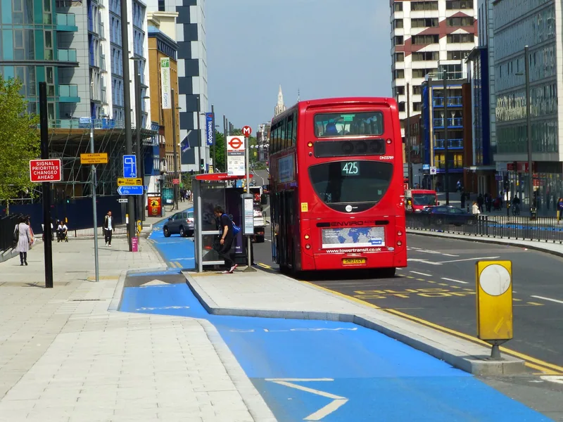 A blue cycle track passing behind an island bus stop where a red double-decker has pulled in