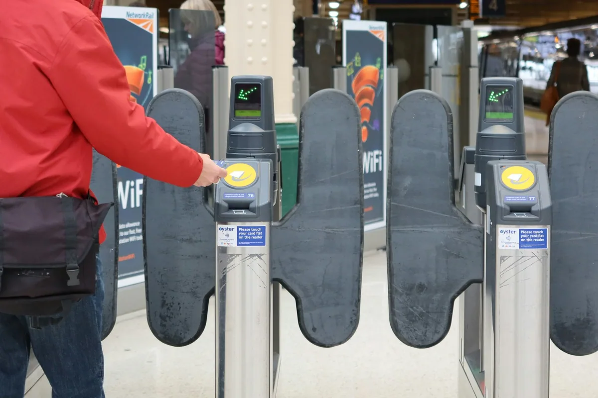 Passenger touching a card on the yellow reader to pass through ticket gates at a London railway station