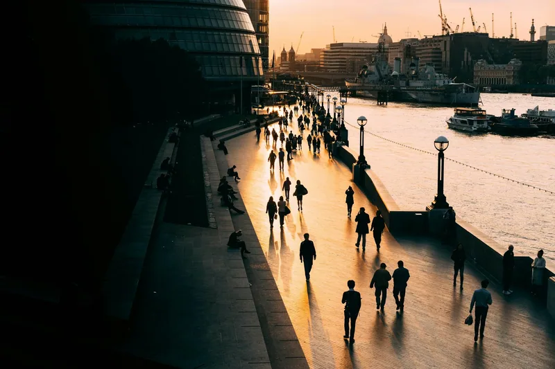 People walking along a Thames riverside path at sunset, seen from above
