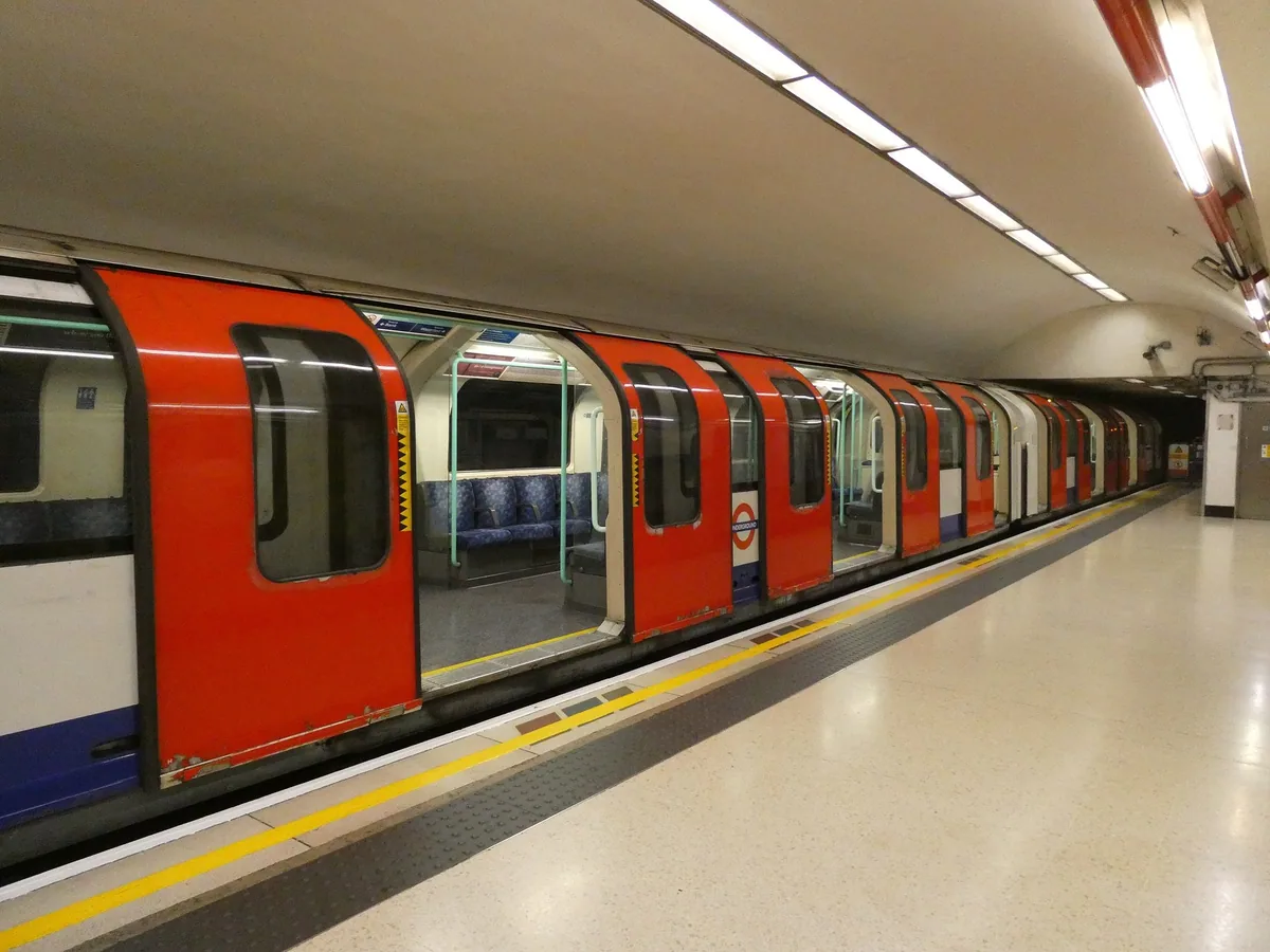 A red 1992 stock Waterloo and City line train standing with its doors open at an empty tube platform