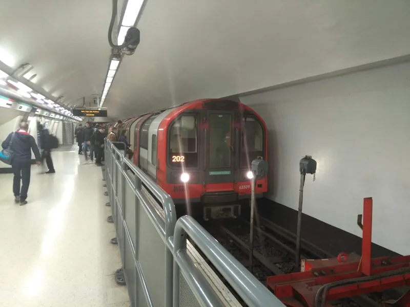 A Waterloo and City line train at the buffer stops in the Bank terminus tunnel, with passengers waiting along the platform