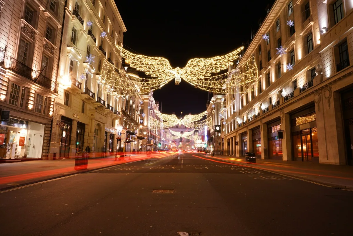 Angel-shaped Christmas lights strung high above a London shopping street at night