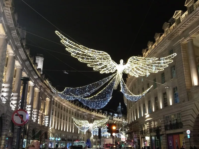 A large illuminated angel of white and blue lights suspended above Regent Street at night