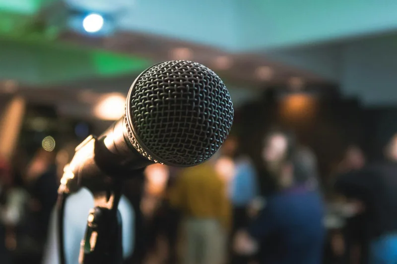 A microphone in close focus on a small stage, with an audience blurred in the background
