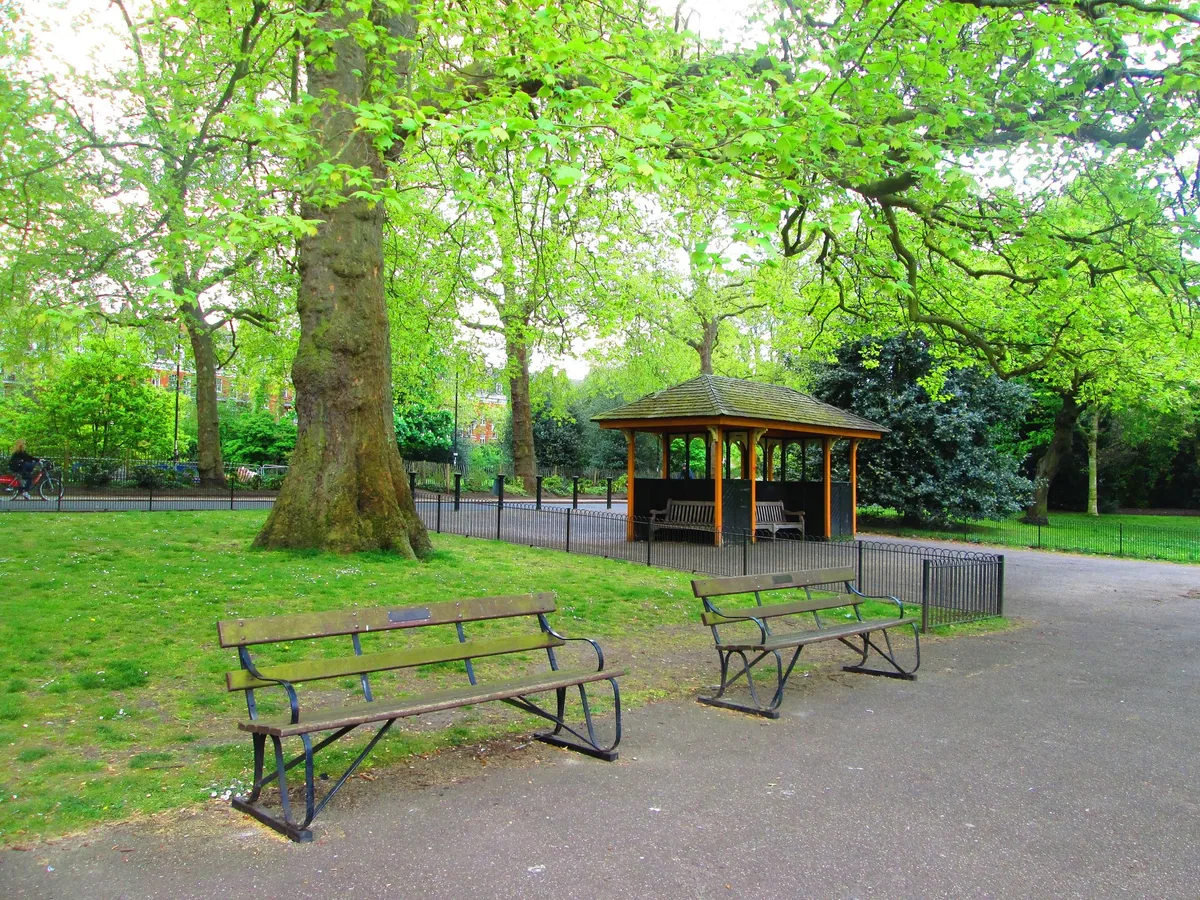 Empty benches and a wooden shelter under fresh green spring trees in Battersea Park
