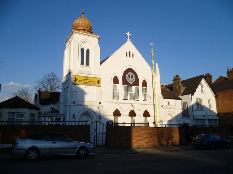 White gurdwara with a golden dome and Sikh Khanda emblem on a north London street