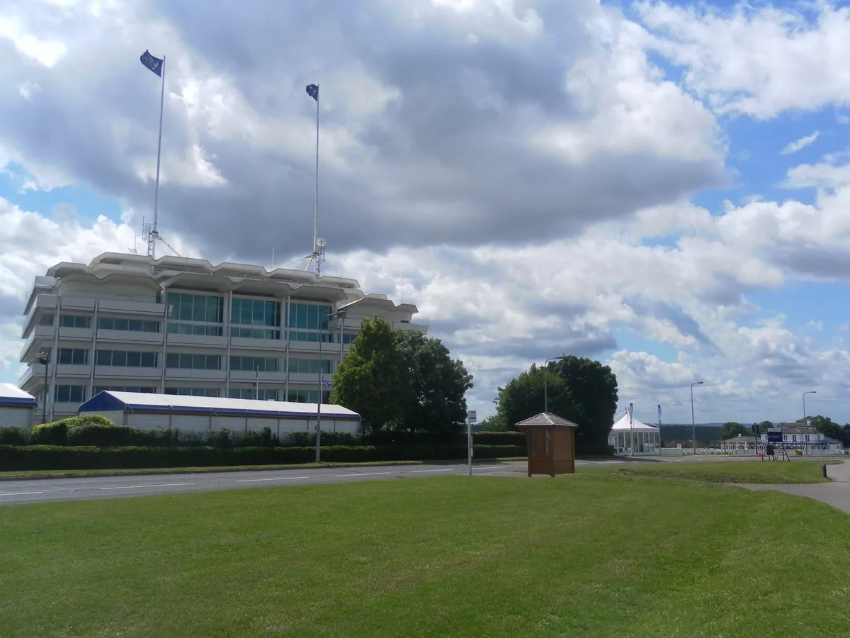The tall glass grandstand at Epsom Downs Racecourse in Surrey, seen across open grass under a cloudy sky