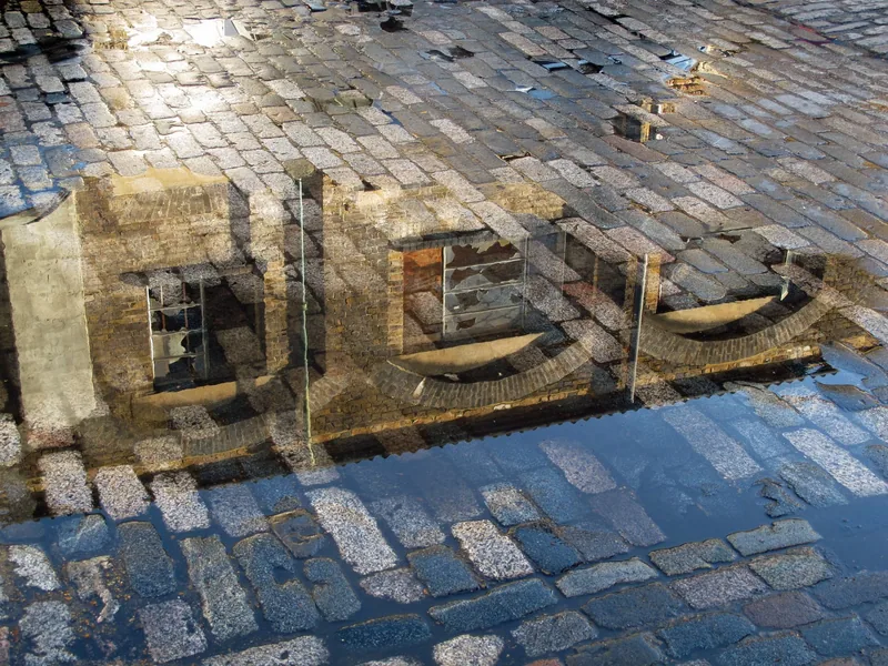Victorian factory windows reflected in a wet cobbled passage in Whitechapel