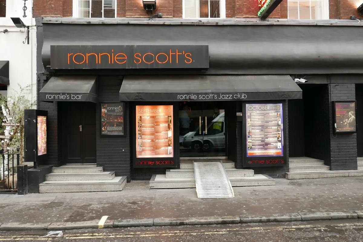 The black shopfront of Ronnie Scott's jazz club on Frith Street in Soho, with its orange neon sign