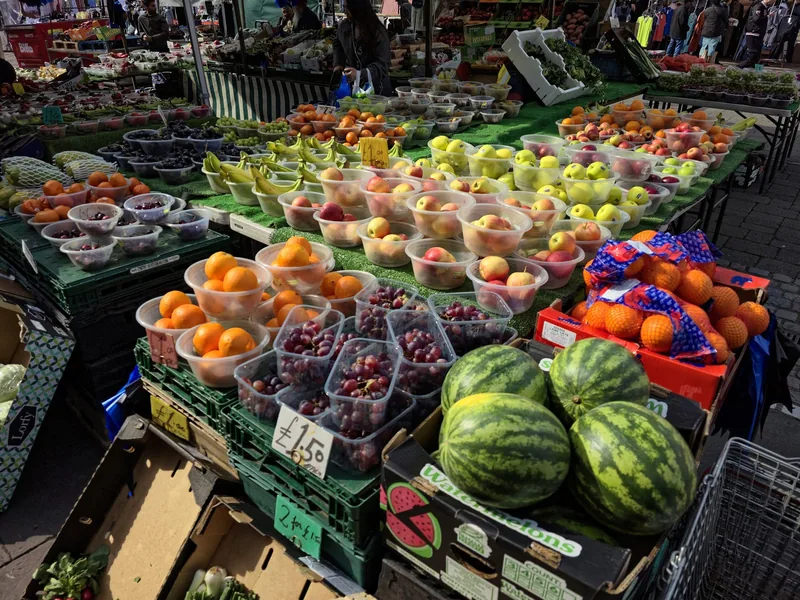 Punnets of fruit and watermelons with handwritten pound prices on an outdoor London market stall