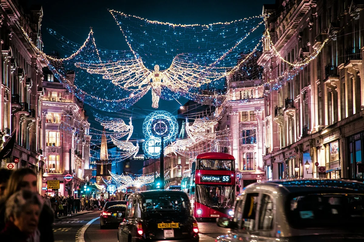 Angel-shaped Christmas lights strung above a London shopping street at night, with a red bus and a black cab below