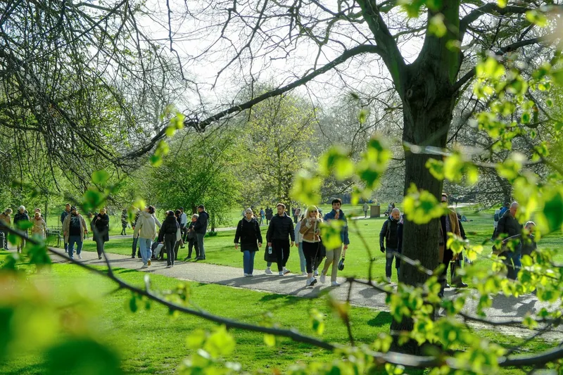 People in coats walking a path through St James's Park as the first leaves open on the trees