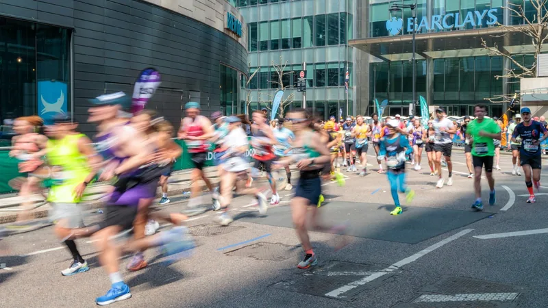 A field of marathon runners on a city street past glass office towers, legs blurred with movement