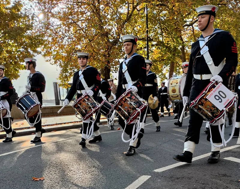 Drummers of a Sea Cadet band marching along a London street under autumn plane trees in the procession